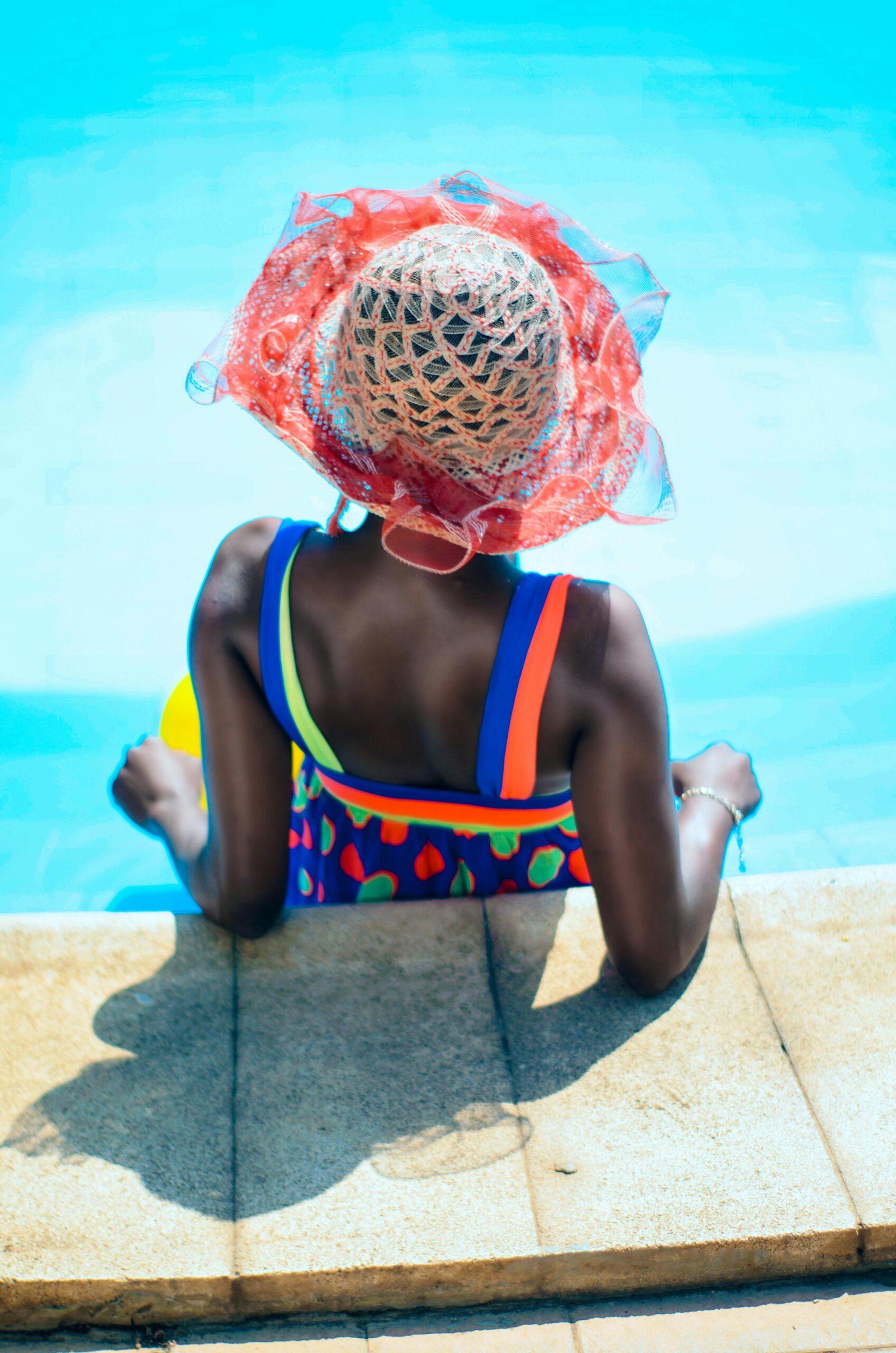 black woman with pink hat and colorful swimsuit at the pool